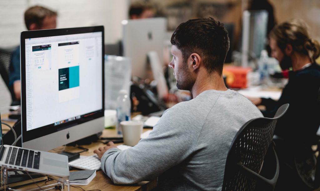 man in gray sweatshirt sitting on chair in front of iMac